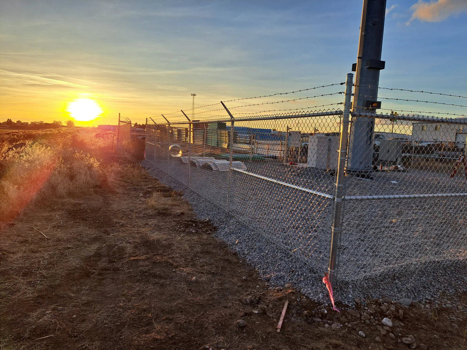 Commercial chain link fence with barbed wire arms at sunrise on an Idaho job site