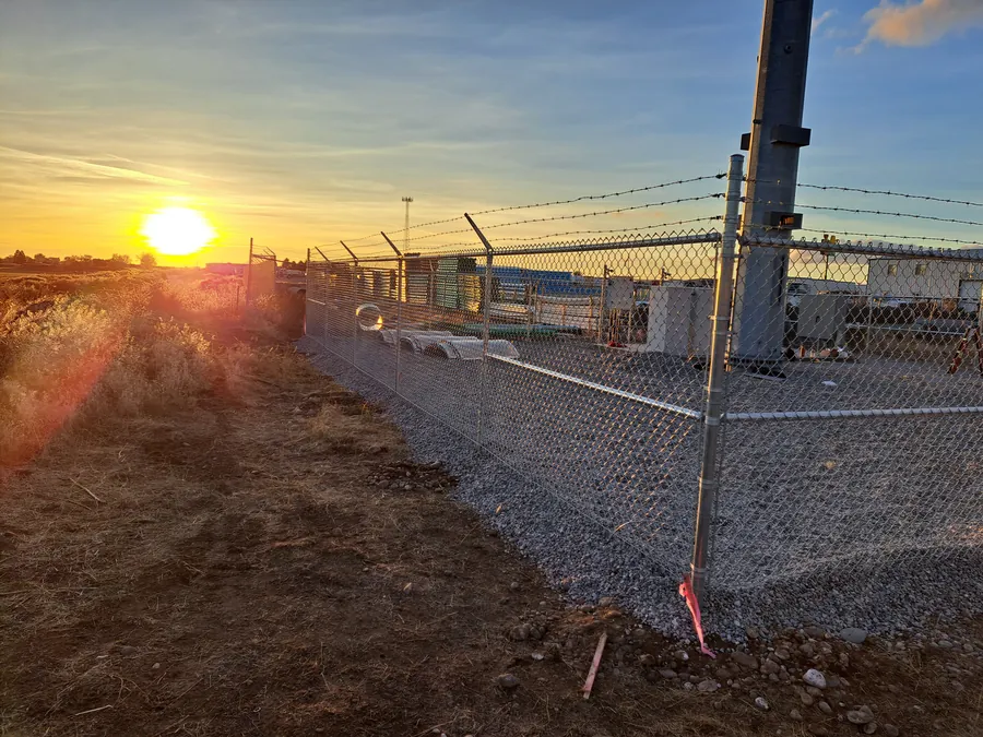 Commercial chain link fence with barbed wire arms at sunrise on an Idaho job site